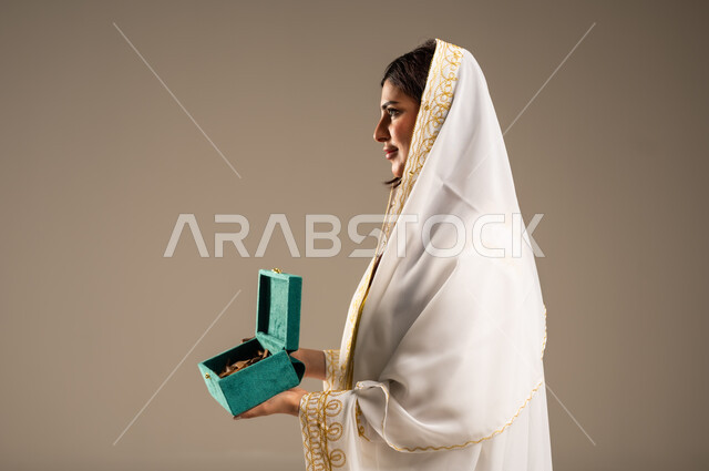 روائح عطرية متميزة، ذكرى تأسيس الدولة السعودية الاولى 22 فبراير، الاحتفال بالمناسبات والأعياد الوطنية، بورتريه مقرب من الجانب لشابة عربية خليجية سعودية ترتدي العباءة البيضاء تحمل بيدها صندوق من خشب العود، يوم بدينا 1727 م، خلفية بيج