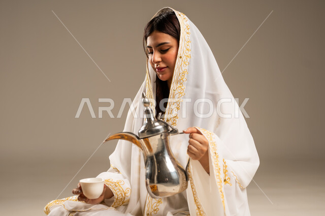 The concept of generosity and hospitality, the day we started 1727 AD, celebrating national occasions and holidays, the anniversary of the founding of the first Saudi state, February 22, a close-up portrait of a young Saudi Arabian Gulf woman wearing a white abaya pouring coffee from a copper pot, beige background