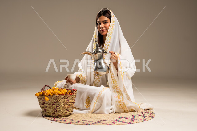Anniversary of the founding of the first Saudi state, February 22, the concept of generosity and good reception, the day we started 1727 AD, a portrait of a young Saudi Gulf Arab woman wearing a white abaya sitting on a straw mat holding a copper coffee pot in her hand, looking at the camera with gestures of pleasure, beige background