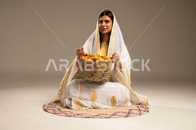 National occasions and holidays, local products and crops, anniversary of the founding of the first Saudi state, February 22, portrait of a young Saudi Gulf Arab woman wearing a white abaya sitting on a straw mat holding a basket full of dates, the day we started 1727 AD, beige background
