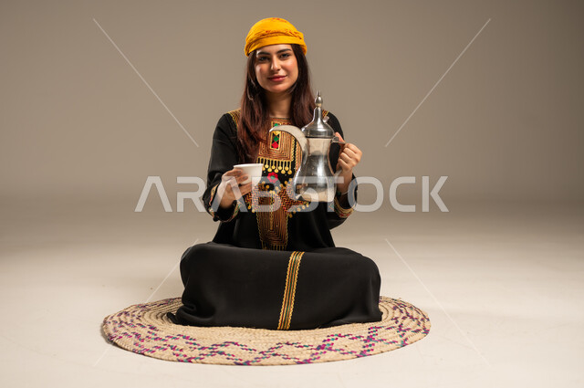 حب الوطن والانتماء اليه، ذكرى تأسيس الدولة السعودية الاولى 22 فبراير، مفهوم الكرم وحسن الاستقبال، يوم بدينا 1727 م، بورتريه لشابة عربية خليجية سعودية ترتدي الشيلة والسدرة تجلس على حصيرة من القش تنظر الى الكاميرا تحمل بيدها الدلة النحاسية والفنجان، خلفية بيج