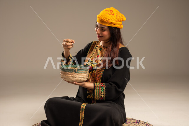 يوم بدينا 1727 م، منتجات ومحاصيل محلية، حب الوطن والانتماء اليه، ذكرى تأسيس الدولة السعودية الاولى 22 فبراير، بورتريه لشابة عربية خليجية سعودية ترتدي الشيلة والسدرة تجلس على حصيرة من القش تحمل بيدها سلة مليئة بالحبوب، المناسبات والأعياد الوطنية، خلفية بيج