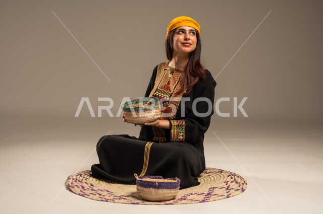 منتجات ومحاصيل محلية، حب الوطن والانتماء اليه، ذكرى تأسيس الدولة السعودية الاولى 22 فبراير، يوم بدينا 1727 م، بورتريه لشابة عربية خليجية سعودية ترتدي الشيلة والسدرة تجلس على حصيرة من القش تحمل بيدها سلة مليئة بالحبوب، المناسبات والأعياد الوطنية، خلفية بيج
