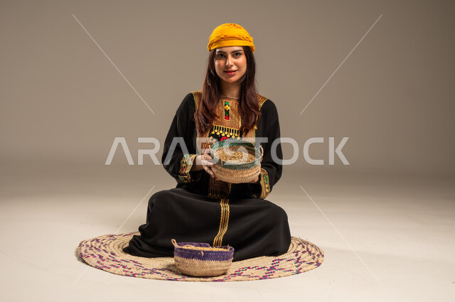 حب الوطن والانتماء اليه، ذكرى تأسيس الدولة السعودية الاولى 22 فبراير، منتجات ومحاصيل محلية، يوم بدينا 1727 م، بورتريه لشابة عربية خليجية سعودية ترتدي الشيلة والسدرة تجلس على حصيرة من القش تنظر الى الكاميرا تحمل بيدها سلة مليئة بالحبوب، خلفية بيج