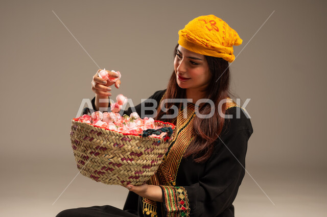 The concept of patriotism and belonging to the homeland, the anniversary of the founding of the first Saudi state, February 22, national occasions and holidays, a close-up portrait of a young Saudi Gulf Arab woman wearing a shayla and a sidr tree, holding a straw basket full of natural roses, the day we began 1727 AD, beige background