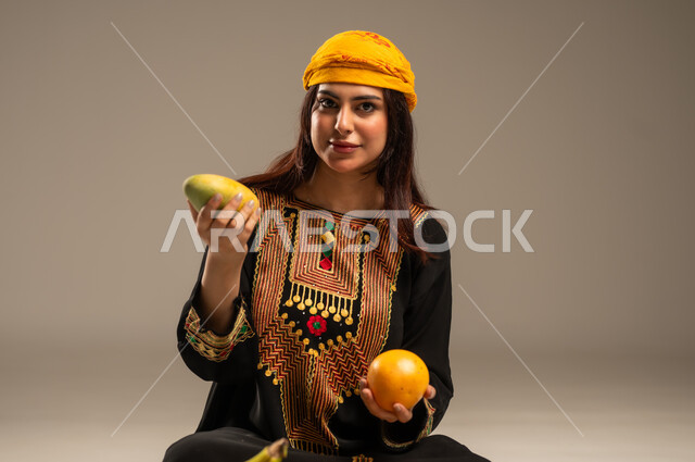 The Day We Began 1727 AD, National Holidays and Occasions, Local Agricultural Crops and Products, Anniversary of the Founding of the First Saudi State February 22, Portrait of a Young Saudi Gulf Arab Woman Wearing a Shayla and a Sidra Tree Looking at the Camera Holding Fresh Fruits in Her Hand, Beige Background