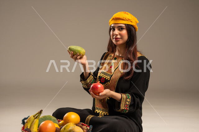National holidays and occasions, local agricultural crops and products, the anniversary of the founding of the first Saudi state, February 22, a portrait of a young Saudi Gulf Arab woman wearing a shayla and a sidr tree looking at the camera holding fresh fruits in her hand, the day we began 1727 AD, beige background