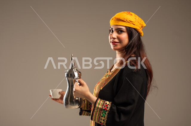 مفهوم الكرم وحسن الاستقبال، حب الوطن والانتماء اليه، ذكرى تأسيس الدولة السعودية الاولى 22 فبراير، يوم بدينا 1727 م، بورتريه مقرب من الجانب لشابة عربية خليجية سعودية ترتدي الشيلة والسدرة تنظر الى الكاميرا تقوم بصب القهوة من الدلة النحاسية، خلفية بيج