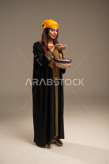 محاصيل ومنتجات محلية، يوم بدينا 1727 م،  ذكرى تأسيس الدولة السعودية الاولى 22 فبراير، الاحتفال بالمناسبات والأعياد الوطنية، بورتريه لشابة عربية خليجية سعودية ترتدي الشيلة والسدرة تحمل بيدها سلة من القش مليئة بالحبوب، صورة الجسم بالطول الكامل، خلفية بيج