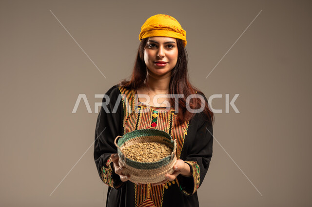 The Day We Began 1727 AD, Local Products and Crops, Anniversary of the Founding of the First Saudi State February 22, Celebrating National Occasions, Close-up portrait of a young Saudi Arabian Gulf woman wearing a Shayla and Sidra tree looking at the camera holding a straw basket full of grains, beige background