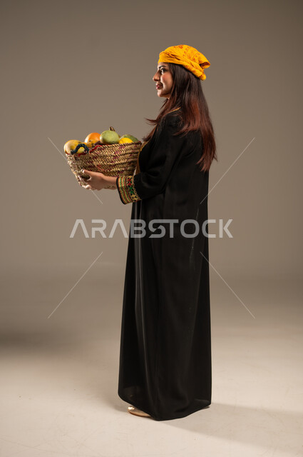 يوم بدينا 1727 م، محاصيل ومنتجات زراعية محلية، ذكرى تأسيس الدولة السعودية الاولى 22 فبراير، بورتريه من الجانب لشابة عربية خليجية سعودية ترتدي الشيلة والسدرة تحمل بيدها سلة من القش مليئة بالفواكه الطازجة، صورة الجسم بالطول الكامل، خلفية بيج