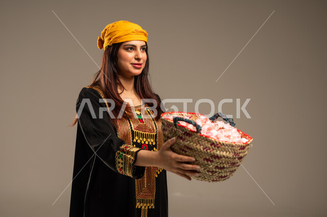 Anniversary of the founding of the first Saudi state, February 22, national occasions and holidays, close-up portrait of a young Saudi Gulf Arab woman wearing a shayla and a sidr tree, holding a straw basket filled with natural roses, the day we began 1727 AD, the concept of love of the homeland and belonging to it, beige background