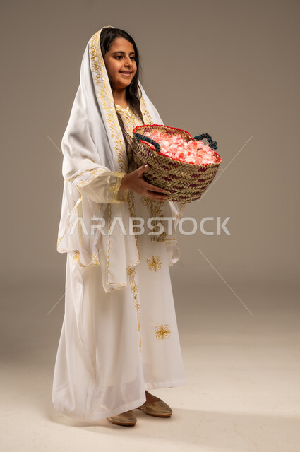 ذكرى تأسيس الدولة السعودية الاولى 22 فبراير، المناسبات والأعياد الوطنية، بورتريه من الجانب لفتاة عربية خليجية سعودية ترتدي الأزياء التراثية تحمل بيدها سلة من الورود، يوم بدينا 1727 م، مفهوم حب الوطن والانتماء اليه، صورة الجسم بالطول الكامل، خلفية بيج