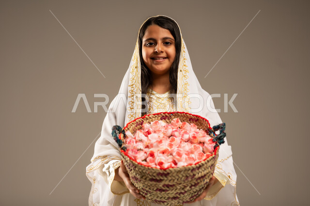 مفهوم حب الوطن والانتماء اليه، الأعياد و المناسبات الوطنية، ذكرى تأسيس الدولة السعودية الاولى 22 فبراير، بورتريه مقرب لفتاة عربية خليجية سعودية مبتسمة ترتدي الأزياء التراثية تنظر الى الكاميرا تحمل بيدها سلة من الورود، يوم بدينا 1727 م، خلفية بيج