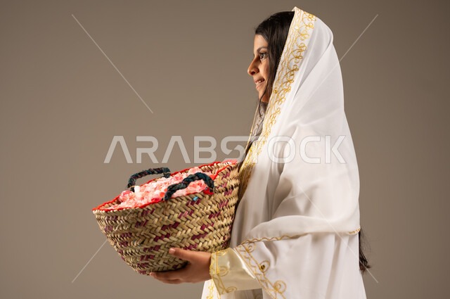 National holidays and occasions, the anniversary of the founding of the first Saudi state, February 22, a close-up portrait from the side of a smiling Saudi Arabian Gulf girl wearing traditional costumes, holding a basket of roses in her hand, the day we began 1727 AD, the concept of love of the homeland and belonging to it, beige background