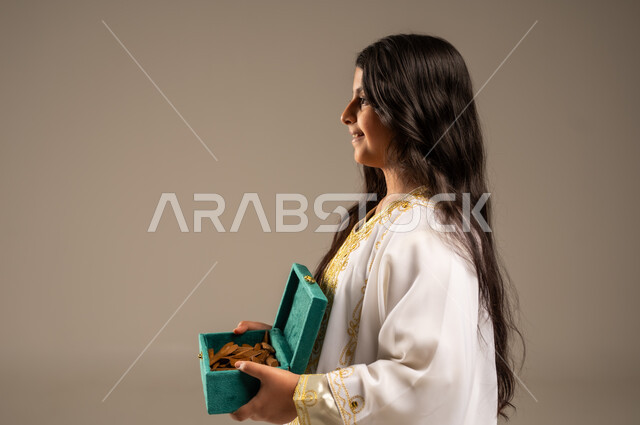 روائح عطرية متميزة، الاحتفال بالمناسبات والأعياد الوطنية، ذكرى تأسيس الدولة السعودية الاولى 22 فبراير، بورتريه مقرب من الجانب لفتاة عربية خليجية سعودية ترتدي العباءة البيضاء تحمل بيدها صندوق من خشب العود، يوم بدينا 1727 م، خلفية بيج