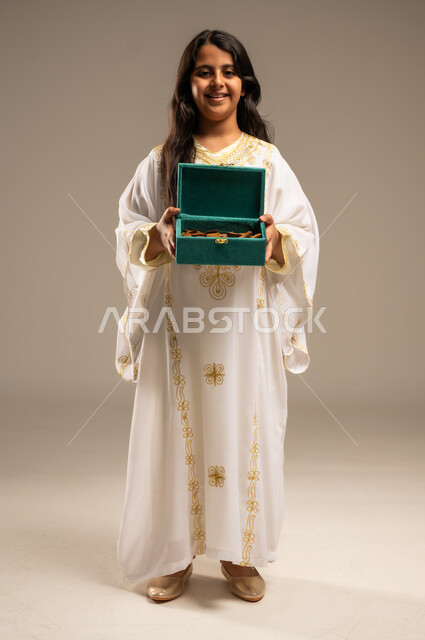 روائح عطرية متميزة، الاحتفال بالمناسبات والأعياد الوطنية، ذكرى تأسيس الدولة السعودية الاولى 22 فبراير، بورتريه لفتاة عربية خليجية سعودية ترتدي العباءة البيضاء تنظر الى الكاميرا تحمل بيدها صندوق من خشب العود، يوم بدينا 1727 م، صورة الجسم بالطول الكامل، خلفية بيج
