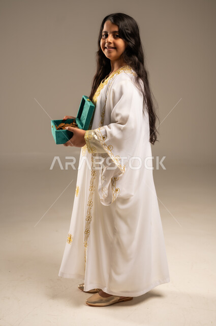 روائح عطرية متميزة، الاحتفال بالمناسبات والأعياد الوطنية، ذكرى تأسيس الدولة السعودية الاولى 22 فبراير، بورتريه لفتاة عربية خليجية سعودية ترتدي العباءة البيضاء تنظر الى الكاميرا تحمل بيدها صندوق من خشب العود، يوم بدينا 1727 م، صورة الجسم بالطول الكامل، خلفية بيج