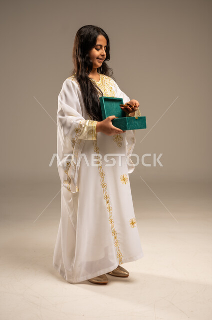 روائح عطرية متميزة، الاحتفال بالمناسبات والأعياد الوطنية، ذكرى تأسيس الدولة السعودية الاولى 22 فبراير، بورتريه لفتاة عربية خليجية سعودية ترتدي العباءة البيضاء تحمل بيدها صندوق من خشب العود، يوم بدينا 1727 م، صورة الجسم بالطول الكامل، خلفية بيج