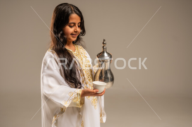 Anniversary of the founding of the first Saudi state February 22, the concept of generosity and good reception, the day we started 1727 AD, celebrating national occasions and holidays, close-up portrait of a Saudi Arabian Gulf girl wearing a white abaya pouring coffee from a copper pot, inheriting authentic customs and traditions, beige background