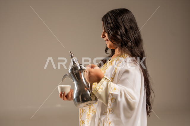 ذكرى تأسيس الدولة السعودية الاولى 22 فبراير، مفهوم الكرم وحسن الاستقبال، يوم بدينا 1727 م، الاحتفال بالمناسبات والأعياد الوطنية، بورتريه مقرب لفتاة عربية خليجية سعودية ترتدي العباءة البيضاء تقوم بصب القهوة من الدلة النحاسية، توارث العادات والتقاليد الأصيلة، خلفية بيج