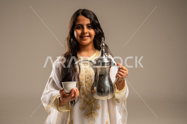 ذكرى تأسيس الدولة السعودية الاولى 22 فبراير، مفهوم الكرم وحسن الاستقبال، يوم بدينا 1727 م، الاحتفال بالمناسبات والأعياد الوطنية، بورتريه مقرب لفتاة عربية خليجية سعودية ترتدي العباءة البيضاء تنظر الى الكاميرا تقوم بصب القهوة من الدلة النحاسية، خلفية بيج