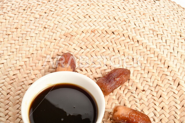 A picture of a bunch of dates next to a bowl of healthy date molasses, a bowl of straw, date honey, healthy and delicious food