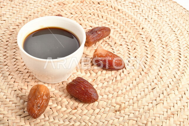 A picture of a bunch of dates next to a bowl of healthy date molasses, a bowl of straw, date honey, healthy and delicious food