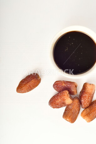 مجموعة من حبات التمر بجانب وعاء دبس التمر الصحي ، خلفية بيضاء ، عسل التمر ، غذاء صحي ولذيذ