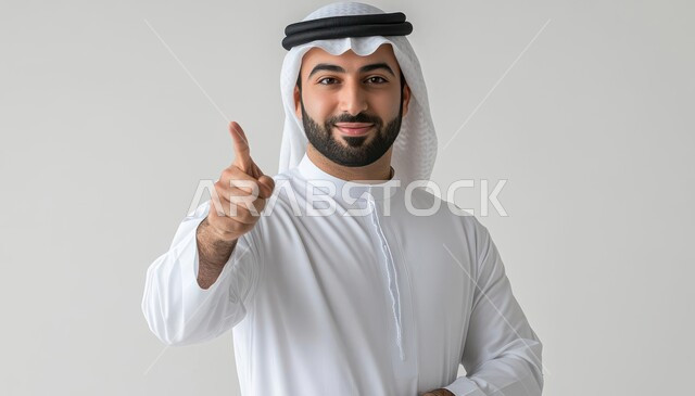 Indicating the location of an item, specifying a specific location, pointing and explaining something, close-up portrait of a young Saudi Arabian Gulf man wearing a traditional thobe and shemagh looking at the camera with gestures of happiness and pleasure and pointing his index finger upwards, gray background