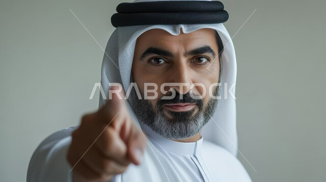 pinpointing a specific location, pointing and explaining something, indicating the location of an item, close-up portrait of a Saudi Arabian Gulf man wearing a traditional thobe and shemagh looking at the camera and pointing his index finger at it, gray background