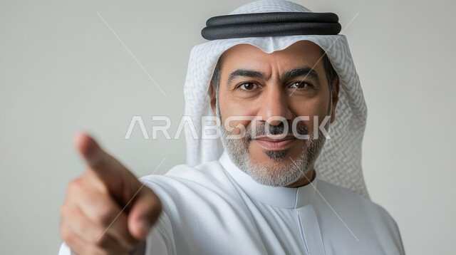 pinpointing a specific location, pointing and explaining something, indicating the location of an item, close-up portrait of a Saudi Arabian Gulf man wearing a traditional thobe and shemagh looking at the camera with gestures of happiness and pleasure and pointing his index finger at it, gray background