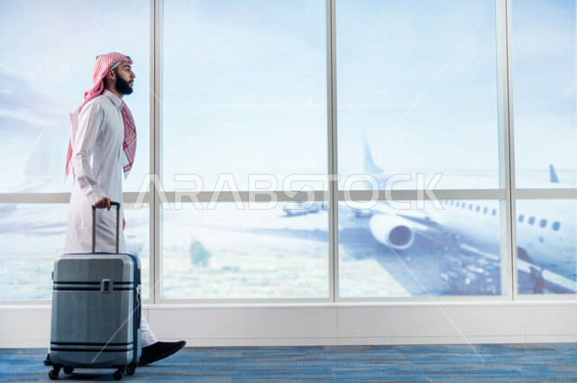 رجل عربي خليجي سعودي، يمسك بحقيبة السفر ويقوم بجرها، الاستعداد للسفر في رحلة عمل، صالة الانتظار في المطار، سياحة وسفر، قضاء أوقات ممتعة
