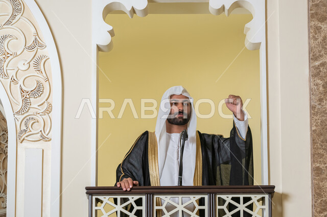 مفهوم العبادة والتقرب إلى الله تعالى, تعزيز الروحانية الجماعية, توجيه الناس نحو الحق والهداية, دور أئمة المساجد والخطباء في نشر الدين، إمام عربي خليجي إماراتي يرتدي البشت والكندورة والغترة البيضاء يقف أمام مكبر الصوت ويلقي الخطبة على المنبر