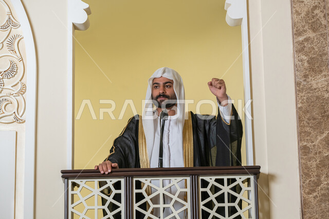 توجيه الناس نحو الحق والهداية, مفهوم العبادة والتقرب إلى الله تعالى, تعزيز الروحانية الجماعية, دور أئمة المساجد والخطباء في نشر الدين، إمام عربي خليجي إماراتي يرتدي البشت والكندورة والغترة البيضاء يقف أمام مكبر الصوت ويلقي الخطبة على المنبر