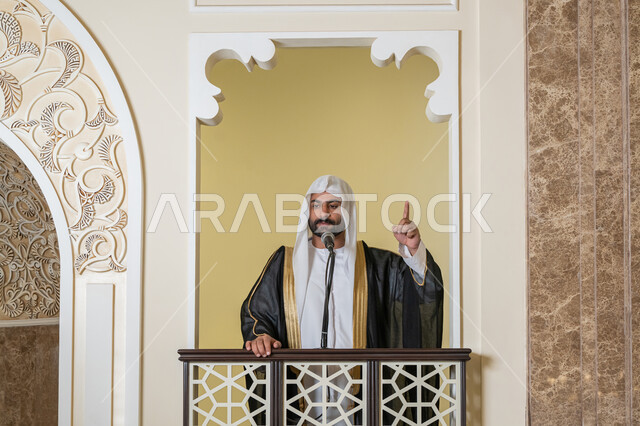 توجيه الناس نحو الحق والهداية, مفهوم العبادة والتقرب إلى الله تعالى, تعزيز الروحانية الجماعية, دور أئمة المساجد والخطباء في نشر الدين، إمام عربي خليجي إماراتي يرتدي البشت والكندورة والغترة البيضاء يقف أمام مكبر الصوت ويلقي الخطبة على المنبر
