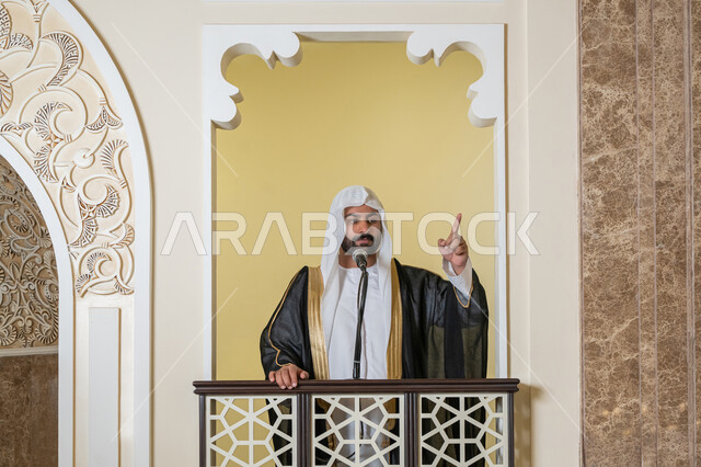 مفهوم العبادة والتقرب إلى الله تعالى, تعزيز الروحانية الجماعية, توجيه الناس نحو الحق والهداية, دور أئمة المساجد والخطباء في نشر الدين، إمام عربي خليجي إماراتي يرتدي البشت والكندورة والغترة البيضاء يقف أمام مكبر الصوت ويلقي الخطبة على المنبر
