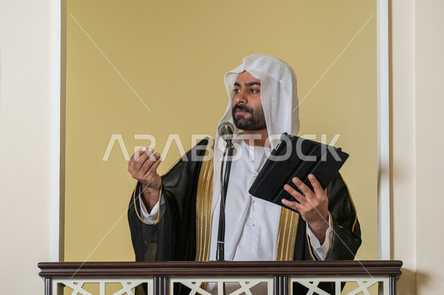 إلقاء خطاب و دروس توجيهية على المسلمين, توجيه الناس لطريق الحق والهداية, الحث على أداء العبادات والفرائض الدينية, إمام مسجد عربي خليجي إماراتي يرتدي البشت والكندورة والغترة البيضاء يقف على المنبر ويلقي خطبة يوم الجمعة من الجهاز اللوحي