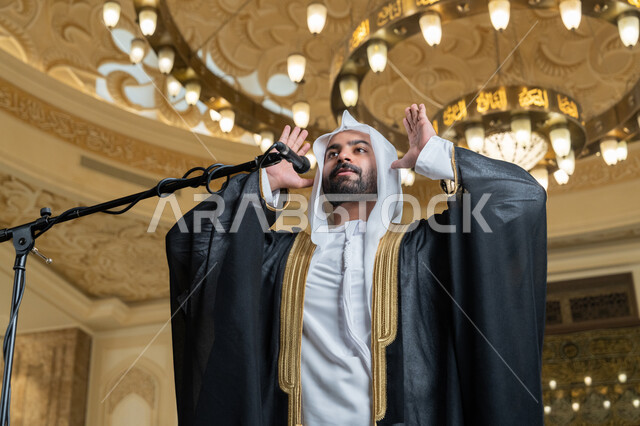الركن الثاني من أركان الإسلام, الشعور بالخشوع والطمأنينة, أداء فرائض الدين الإسلامي, إمامة المسلمين في المسجد, إقامة الصلاة على وقتها، صورة مقربة لإمام عربي خليجي إماراتي يرتدي البشت والكندورة والغترة البيضاء يقوم بأداء فريضة الصلاة ويرفع يديه لتكبيرة الإحرام