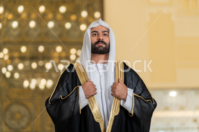 الاهتمام بالمظهر الخارجي، صورة لرجل عربي خليجي اماراتي يرتدي البشت الاسود والغترة البيضاء يقوم بترتيب وتعديل وملابسه، ايماءات الثقة والاعتزاز بالنفس، مفهوم الاناقه والرجولة، الوقوف باستقامة وانضباط