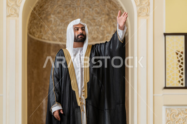 إلقاء التحيه والسلام, مفهوم الاستقبال والترحيب، صورة لرجل عربي خليجي إماراتي يرتدي البشت الاسود والغترة البيضاء ينظر يرفع يده للأعلى بإيماءات المصافحة، التعارف و الصداقه وتكوين العلاقات، مفهوم الاناقة والاهتمام بالمظهر الخارجي