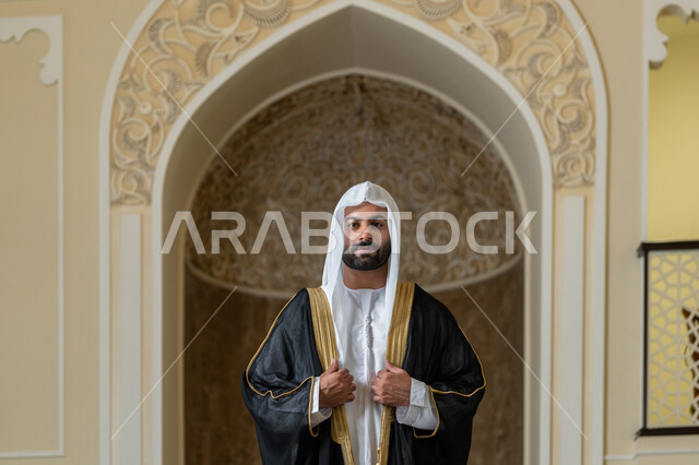 مفهوم الاناقه والرجولة، الاهتمام بالمظهر الخارجي، صورة لرجل عربي خليجي اماراتي يرتدي البشت الاسود والغترة البيضاء يقوم بترتيب وتعديل وملابسه، ايماءات الثقة والاعتزاز بالنفس، الوقوف باستقامة وانضباط