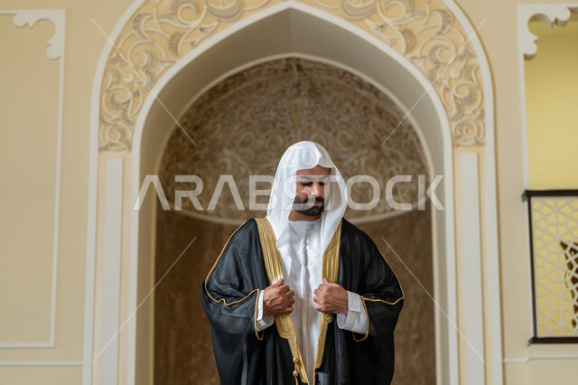 الاهتمام بالمظهر الخارجي، صورة لرجل عربي خليجي اماراتي يرتدي البشت الاسود والغترة البيضاء يقوم بترتيب وتعديل وملابسه، ايماءات الثقة والاعتزاز بالنفس، مفهوم الاناقه والرجولة، الوقوف باستقامة وانضباط