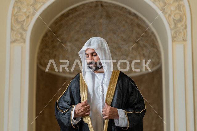 الاهتمام بالمظهر الخارجي، صورة لرجل عربي خليجي اماراتي يرتدي البشت الاسود والغترة البيضاء يقوم بترتيب وتعديل وملابسه، ايماءات الثقة والاعتزاز بالنفس، مفهوم الاناقه والرجولة، الوقوف باستقامة وانضباط