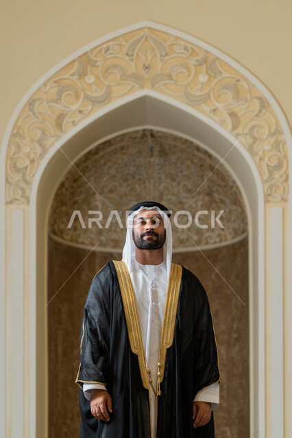 الوقوف باستقامة وانضباط، مفهوم الاناقه والرجولة، الاهتمام بالمظهر الخارجي، صورة لرجل عربي خليجي اماراتي يرتدي البشت الاسود والغترة البيضاء يقوم بترتيب وتعديل وملابسه، ايماءات الثقة والاعتزاز بالنفس
