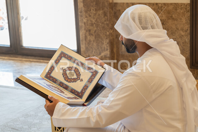 مفهوم العبادة والطاعة والتقرب الى الله, التمعن بسور القرآن الكريم, تدبر الآيات القرآنية والتفكر بها، الالتزام بالورد اليومي, رجل عربي خليجي إماراتي يرتدي الكندورة والغترة البيضاء يجلس في المسجد ويقرأ من المصحف الشريف, التعبد في بيوت الرحمن