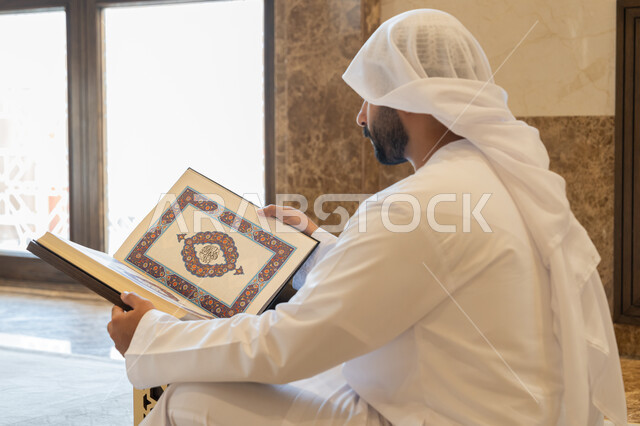 التمعن بسور القرآن الكريم, مفهوم العبادة والطاعة والتقرب الى الله, تدبر الآيات القرآنية والتفكر بها، الالتزام بالورد اليومي, رجل عربي خليجي إماراتي يرتدي الكندورة والغترة البيضاء يجلس في المسجد ويقرأ من المصحف الشريف, التعبد في بيوت الرحمن