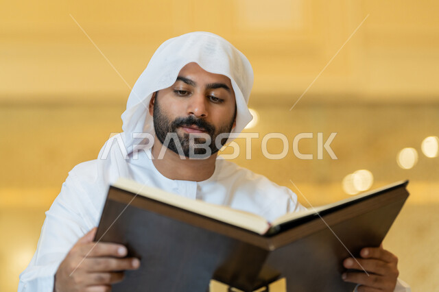 مفهوم العبادة والطاعة والتقرب الى الله, التمعن بسور القرآن الكريم, تدبر الآيات القرآنية والتفكر بها، الالتزام بالورد اليومي, رجل عربي خليجي إماراتي يرتدي الكندورة والغترة البيضاء يجلس في المسجد ويقرأ من المصحف الشريف, التعبد في بيوت الرحمن