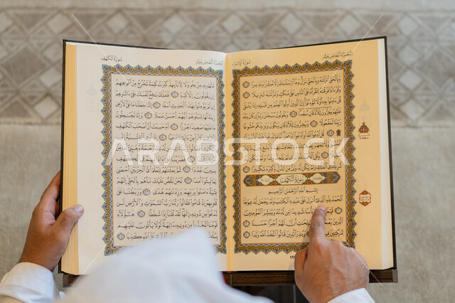 قراءة الورد اليومي, العبادة والطاعة والتقرب الى الله,  تدبر الآيات القرآنية والتفكر بها, صورة من الاعلى لرجل عربي خليجي إماراتي يرتدي الكندورة والغترة البيضاء يجلس في المسجد ويقرأ من المصحف الشريف، التمعن بسور القرآن الكريم، التعبد في بيوت الرحمن