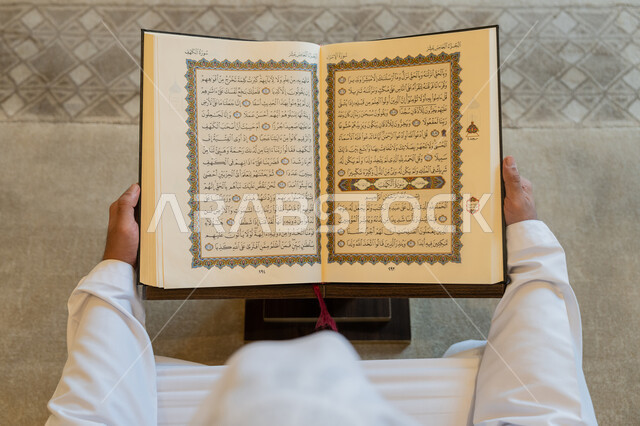 قراءة الورد اليومي, العبادة والطاعة والتقرب الى الله,  تدبر الآيات القرآنية والتفكر بها, صورة من الاعلى لرجل عربي خليجي إماراتي يرتدي الكندورة والغترة البيضاء يجلس في المسجد ويقرأ من المصحف الشريف، التمعن بسور القرآن الكريم، التعبد في بيوت الرحمن